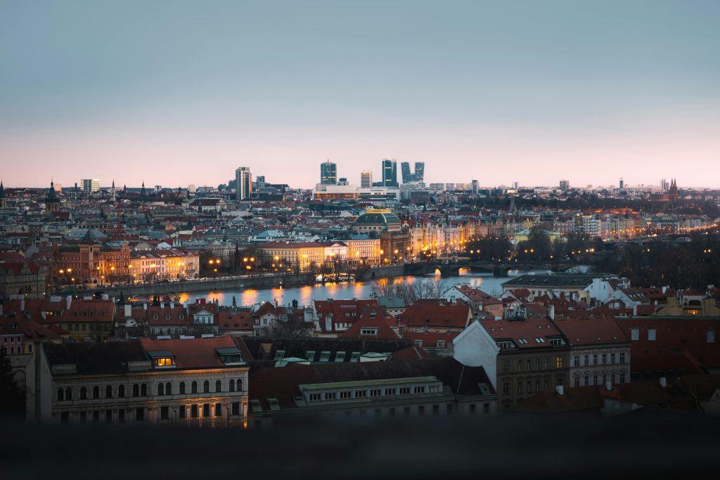 Panoramic view of Prague cityscape at dusk, highlighting Vltava river and historical buildings.